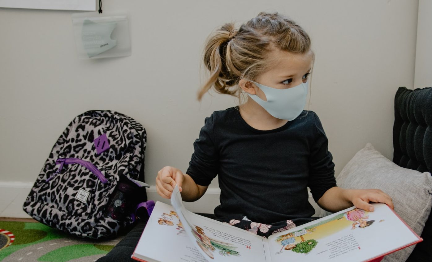 Une enfant à l'école primaire avec un couvre-visage qui lit un livre 