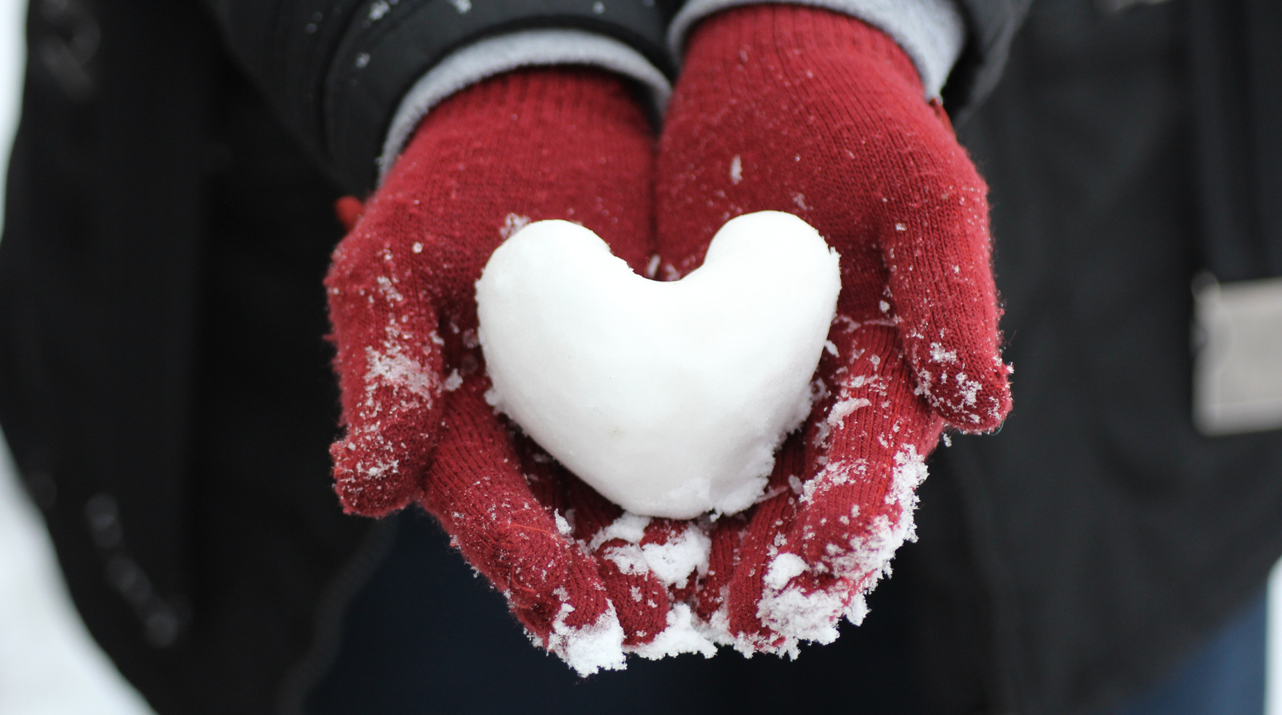 Une personne qui tient au creux de ses mains un coeur fait de neige 