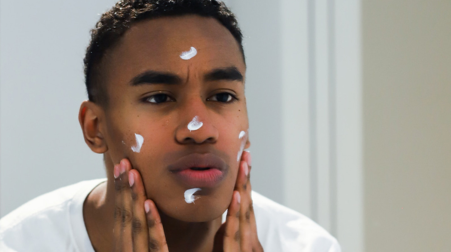 jeune homme en train d'appliquer de la crème sur son visage 
